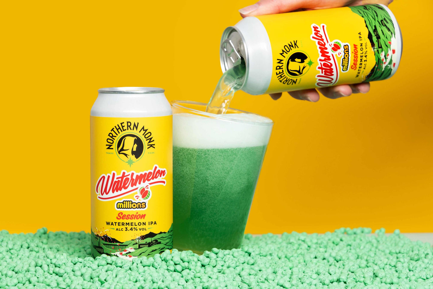 Cans of Northern Monk Watermelon Millions Session IPA being poured into a glass, surrounded by chewy sweets, on a vibrant yellow background.